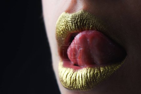 Téléchargez les photos : La langue sexy lèche les lèvres. Lèvres dorées avec rouge à lèvres métallique créatif. Lèvre en métal doré. Femme sensuelle bouche, gros plan, macro - en image libre de droit
