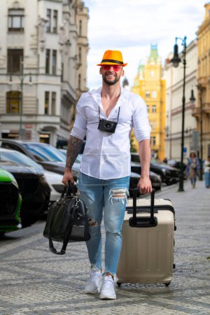 Foto de Estudiante viajero o joven turista. Hombre viajero con bolsa de viaje al aire libre. Retrato de hombre joven caucásico en sombrero y gafas de sol en las vacaciones de verano - Imagen libre de derechos