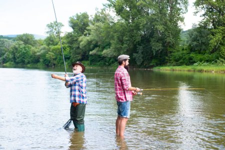 Téléchargez les photos : Père et fils mature pêcheur pêche avec une canne à pêche sur la rivière - en image libre de droit