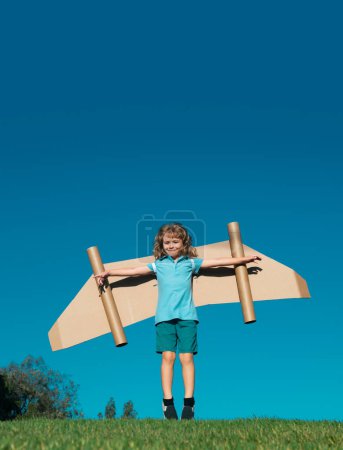 Foto de Pequeño niño juega astronauta o piloto. Niño en el fondo del cielo azul. Niños con alas de papel jetpack sueños. Los niños imaginan sueños de volar. Chico gracioso con mochila de juguete. Éxito, imaginación - Imagen libre de derechos