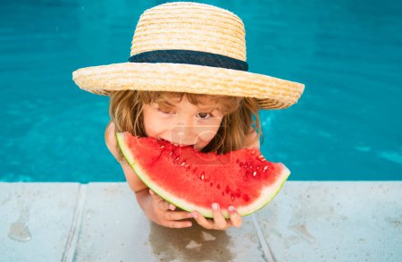 Téléchargez les photos : Mignon petit garçon dans la piscine mangeant pastèque. Profitez de manger des fruits tropicaux. Concept pour enfants d'été. Bonne enfance - en image libre de droit