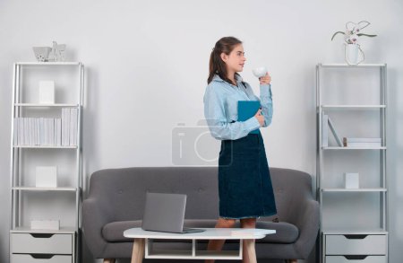 Téléchargez les photos : Jeune femme d'affaires avec une tasse de café au bureau. Secrétaire femme en tenue formelle travaillant sur le projet au bureau moderne - en image libre de droit