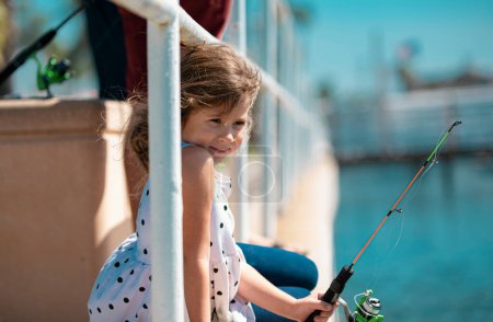 Foto de Una niña pequeña se sienta en el lago, sueña. Cálido día de verano o primavera. Linda pesca niño caucásico - Imagen libre de derechos
