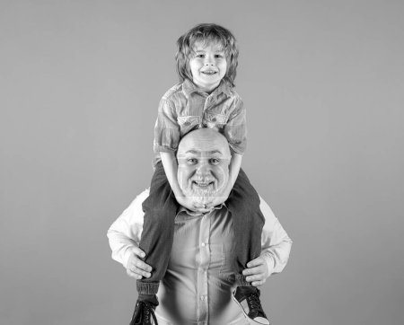 Photo for Grandfather and grandson piggyback ride with funny face isolated on blue in studio - Royalty Free Image
