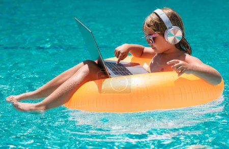 Téléchargez les photos : Travail en ligne et se détendre dans la piscine. Enfant travaillant sur ordinateur portable à la piscine. Technologie en ligne d'été - en image libre de droit