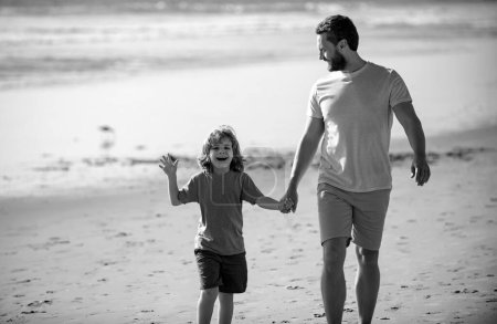 Téléchargez les photos : Père et fils marchant sur la plage d'été. Papa et enfant garçon se tiennent la main et marchent ensemble. Voyage en famille, vacances, concept de fête des pères - en image libre de droit