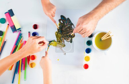 Foto de Desk of an artist hands with drawing painting colorful paints and pencil crayons on white background. Kids learning painting - Imagen libre de derechos