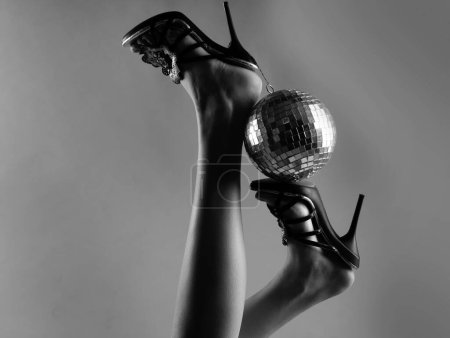 Sexy woman legs. Disco party event. Woman high heels with gold disco ball. Celebrating background
