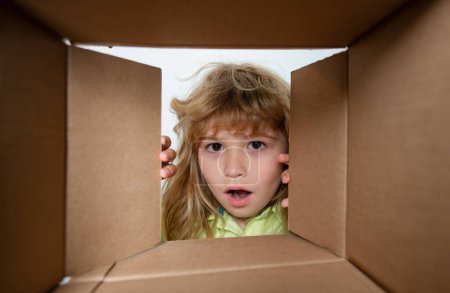 Kid boy unpacking and opening carton box looking inside with surprise face. Kid opening package