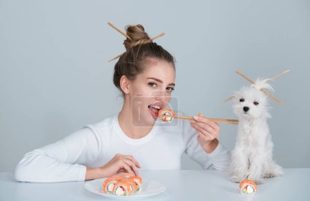 Foto de Estilo sushi japonés. Mujer sexy comer rollos de sushi comida tradicional japonesa. Chica está sosteniendo pedazo de sushi japonés de rollo filadelfia por palillos. Publicidad con perro mascota - Imagen libre de derechos
