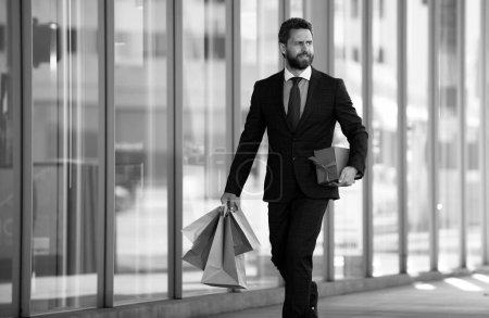Téléchargez les photos : Homme d'affaires tenant des sacs à provisions et marchant dans un magasin. Faire du shopping et payer. Magasins concept de shopping - en image libre de droit