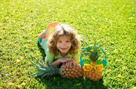 Photo for Little blonde kid hugging pineapple on nature background. Childhood, healthy nutrition, advertising. Close up kids funny face, copy space - Royalty Free Image