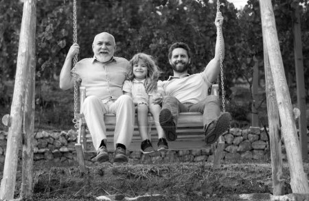 Hombres familia jugando en swing juntos Emocionado abuelo, padre sorprendido y divertido hijo balanceándose juntos en el parque al aire libre. Concepto del día de los padres. Concepto de generación