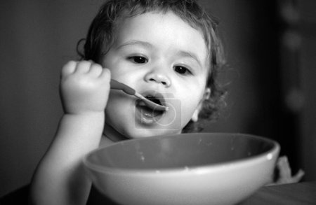 Téléchargez les photos : Drôle petit bébé dans la cuisine manger avec les doigts de la plaque - en image libre de droit