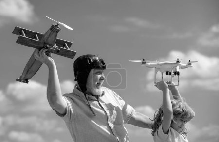 Téléchargez les photos : Vieux grand-père et jeune petit-fils enfant avec avion et drone quadcopter sur fond bleu ciel et nuages. Hommes génération grand-père et petit-enfant - en image libre de droit