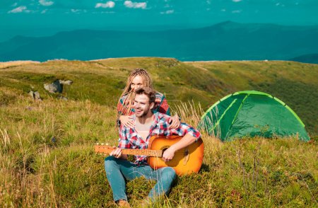 Foto de Pareja romántica acampando en paisaje primaveral. Aventura para los amantes jóvenes campistas en la naturaleza, hombre con guitarra - Imagen libre de derechos