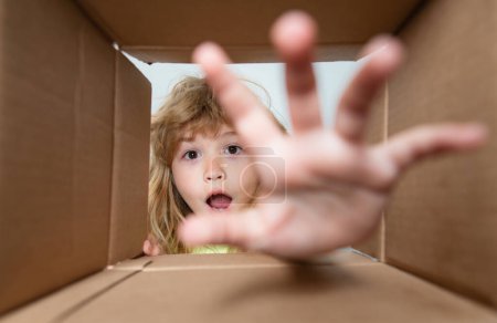 Photo for Child boy opening a carton box and looking inside, take by hand gift. Unpacking concept, surprise unboxing. Parcels and delivery - Royalty Free Image