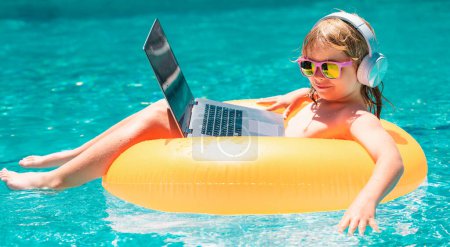 Téléchargez les photos : Enfant travaillant sur ordinateur portable à la piscine. Affaires d'été et technologie en ligne - en image libre de droit