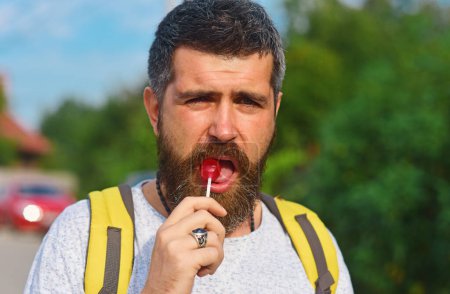 Foto de Hiker man with backpack hiking in beautiful forest. Gay lick lollipop - Imagen libre de derechos