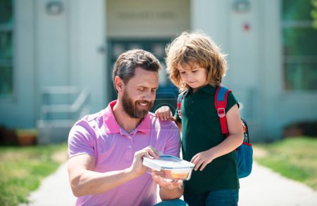 Photo for School boy going to school with father. Schoolboy and parent in shirt holding lunch box. School lunch for kids - Royalty Free Image