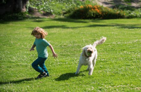 Foto de Un niño divertido corre con un perro. Niño feliz jugando con el perro en el jardín. Niño corriendo con un perro en el parque - Imagen libre de derechos