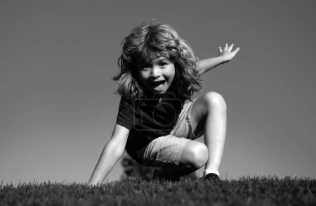 Téléchargez les photos : Joyeux petit enfant blond allongé sur l'herbe dans le parc. Journée plus chaude pendant les vacances scolaires. Enfant incroyable garçon rêvant et souriant en plein air - en image libre de droit