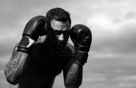 Téléchargez les photos : La boxe sportive. boxeur sportif combattant sur fond de ciel. Homme athlétique fort avec des gants de boxe poinçonnant. Punch de boxe - en image libre de droit
