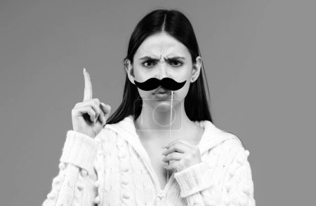 Téléchargez les photos : Une femme avec une fausse moustache qui s'amuse. Drôle d'actrice féminine avec doigt vers le haut isolé sur fond bleu - en image libre de droit