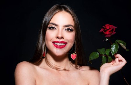 Téléchargez les photos : Femme souriante avec épaule nue lèvres rouges et fleur de rose. Mode beauté portrait sur fond noir studio - en image libre de droit
