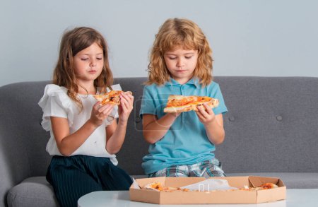 Photo for Cute little kids boy and girl eating Pizza at home. Children holding a slices of pizza on party at home. Two young children bite pizza indoors - Royalty Free Image