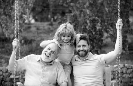 Großvater mit Sohn und Enkel auf einer Schaukel im Frühlingsgarten im Freien. Aktive Freizeitaktivität für die Familie. Mehrgenerationenfamilie