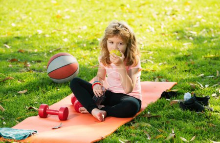 Photo for Healthy lifestyle and healthy food concept. Little boy child in sportswear eating apple sitting on sport mat after training on sunny spring day. Healthy kids lifestyle - Royalty Free Image