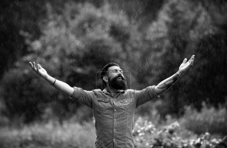 Téléchargez les photos : Il pleut. Homme sous la pluie d'été. Portrait d'homme barbu heureux insouciant sur la nature. Optimisme adulte et temps seul - en image libre de droit
