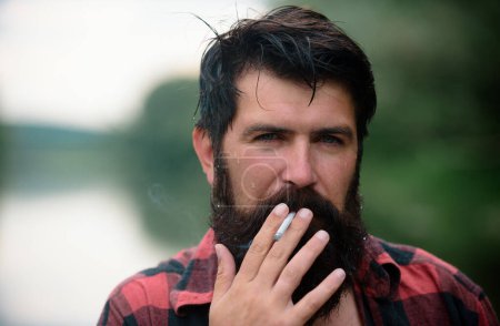 Téléchargez les photos : Fumer homme barbu en plein air. Mauvaise habitude, dépendance à la cigarette - en image libre de droit