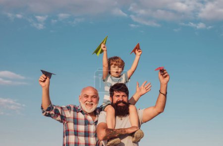 Foto de Feliz niño sonriente en el hombro papá mirando a la cámara. Familia feliz. Aviador piloto infantil con avión de papel sueña con viajar. Concepto de generación - Imagen libre de derechos