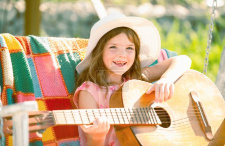 Photo for Happy smiling child girl play the guitar. Kids music and songs. Smiling child playing outdoors in summer - Royalty Free Image