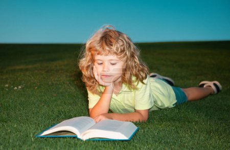 Foto de El colegial con el libro descansando al aire libre. Niño con un libro en el jardín. Kid está leyendo un libro jugando al aire libre en el día de verano - Imagen libre de derechos