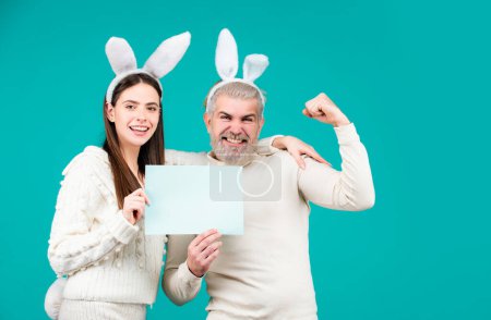 Foto de Pareja de Pascua vestida con traje sosteniendo la pizarra blanca en blanco para su texto. Conejito de Pascua pareja sobre fondo azul aislado - Imagen libre de derechos