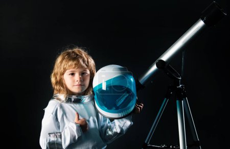 Téléchargez les photos : Un gamin qui explore l'espace. Portrait d'enfants mignons en costumes spatiaux avec un télescope. Concept de journée Cosmonautique. Concept d'astronomie et d'astrologie - en image libre de droit