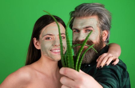 Téléchargez les photos : Masque visage vert pour couple amusant. Couple drôle obtenir des soins du visage avec aloe vera. Esthéticienne fait masque facial sur le visage de l'homme et de la femme. Cosmétologue faire une procédure faciale avec aloe vera - en image libre de droit