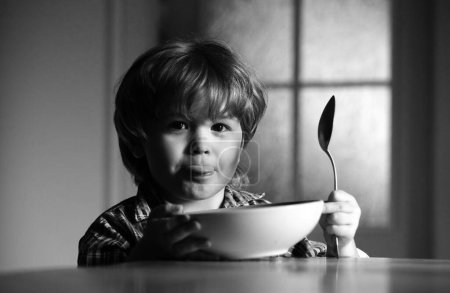 Foto de Bebé comiendo comida en la cocina. Un chico lindo está comiendo. Riéndose niño lindo bebé niño sentado en trona y comiendo sobre fondo borroso - Imagen libre de derechos