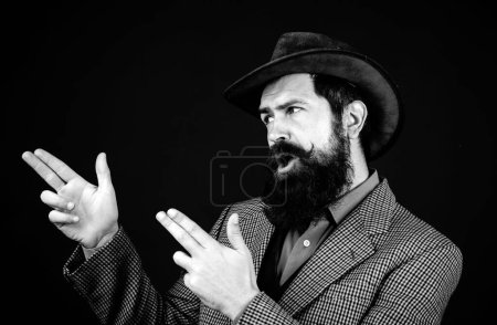 Foto de Vaquero barbudo con traje y sombrero aislado en fondo negro. Hipster hombre seguro de sí mismo con traje de estilo retro y sombrero. Hombre gesticulativo barbudo fresco - Imagen libre de derechos