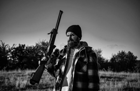 Hunter con escopeta a la caza. Barbudo cazador hombre sosteniendo arma y caminando en el bosque
