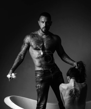 Photo for Dominantning in the foreplay sexual game. Tattooed couple. Tattooed man and woman have fun in the bathroom and he washes her beautiful back. Dominant concept - Royalty Free Image