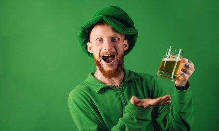 Fiesta del día de Patricks. Retrato de un hombre excitado sosteniendo un vaso de cerveza en el día de San Patricio aislado en verde. Hombre en traje de Patricks sonriendo
