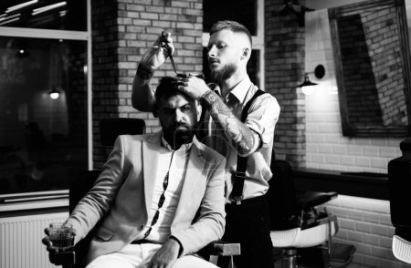 Foto de Tijeras de barbero y navaja de afeitar. Peluquero afeitando a un barbudo en una peluquería. Barbudo hombre consiguiendo corte de pelo por peluquería y sentado en silla en la barbería - Imagen libre de derechos