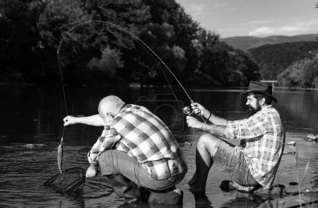 Téléchargez les photos : Pêche à la mouche dans la nature sauvage vierge du Canada. Pêcheur pêchant dans une rivière avec une canne à pêche. Générations âges : grand-père et père - en image libre de droit
