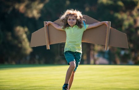 Téléchargez les photos : Les enfants volent. Enfant pilote drôle volant avec des ailes d'avion en carton jouet dans le parc, l'espace de copie. Démarrer concept de liberté, enfant insouciant - en image libre de droit