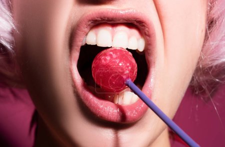 Téléchargez les photos : Gros plan lèvres femelles avec rouge à lèvres rose tenant dans la bouche sucette bonbons rouges. Sucette sur un visage - en image libre de droit