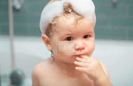 Téléchargez les photos : Bébé enfant se lave dans une salle de bain en mousse. Les enfants drôles font face de près. Bain d'enfant dans la baignoire - en image libre de droit